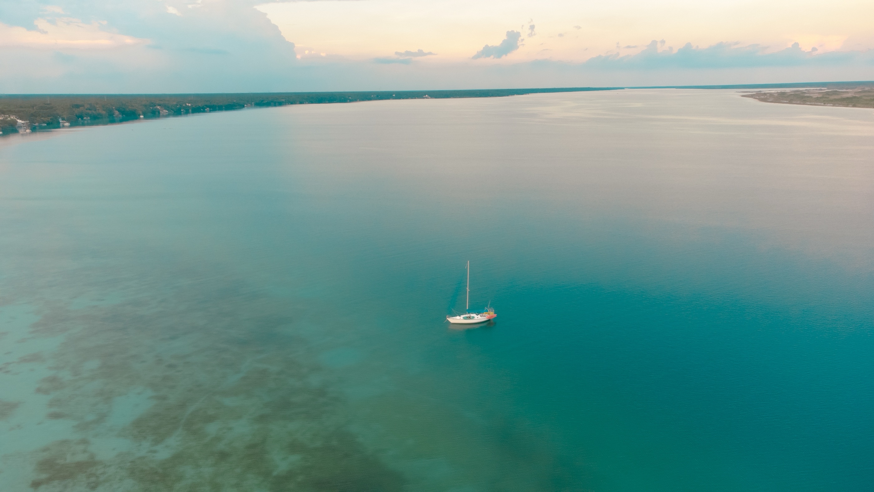 Voilier au mouillage sur les eaux turquoise de la lagune au crépuscule.